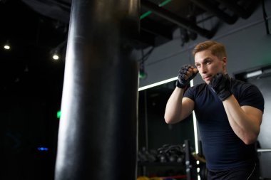 Genç boksör siyah kum torbasıyla antrenman yapıyor.