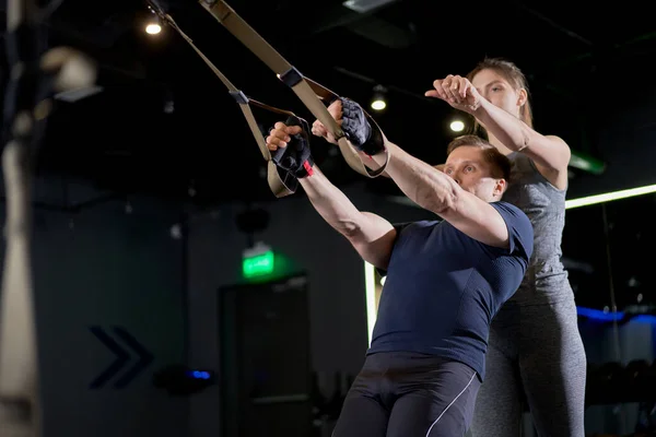 Hombre atlético en entrenamiento con bandas elásticas con entrenador de mujer — Foto de Stock