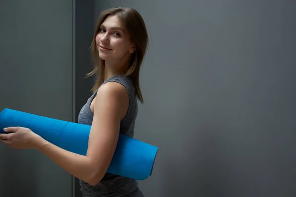 Deportiva chica con alfombra azul en las manos en el fondo de la pared gris — Foto de Stock