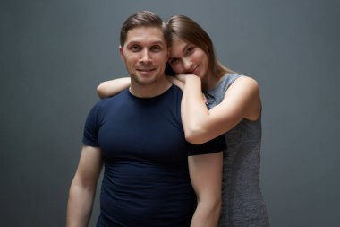 Stüdyodaki gri duvarın arkasında sarılan adam ve kadın.