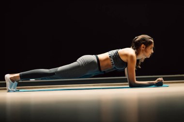 Spor salonundaki halının üzerinde tahta bir poz vermiş genç bir kadın.