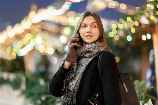 갈런드의 흐릿 한 배경 속에서 저녁에 손에 핸드폰을 들고 거리에 있는 여성의 사진 — 스톡 사진