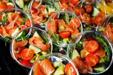 İçinde kırmızı balık salatası, domates, salatalık, otlar olan açık büfe masasının tepesinde.