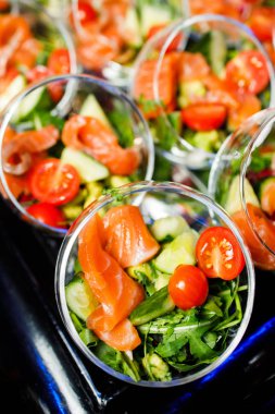 Açık büfenin üstünde kırmızı balık salatası, domates ve salatalık var.