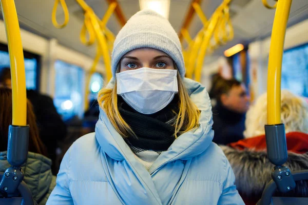 Chica en máscara médica de pie en el salón de autobuses junto a pasamanos amarillos por la tarde . — Foto de Stock