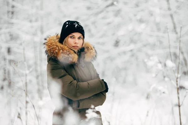 Ung flicka tittar på kameran på bakgrund av snöiga träd på promenad i vinterskogen — Stockfoto