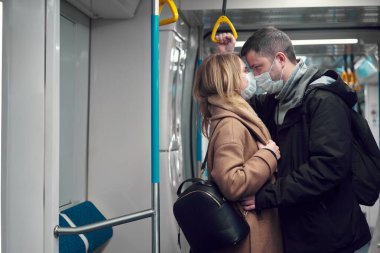 Metroda maskeli genç bir çift sarılıyor..