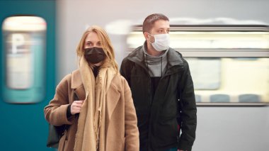 Tıbbi maskeli bir adam ve sarışın kadın metroda arabanın yanında duruyor..