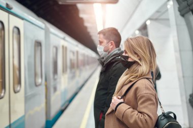 Tıbbi maskeli bir adam ve kadın metroda at arabasının yanında dikiliyorlar..