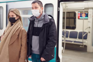 Tıbbi maskeli genç adam ve kadın metro vagonunun yanında duruyor..
