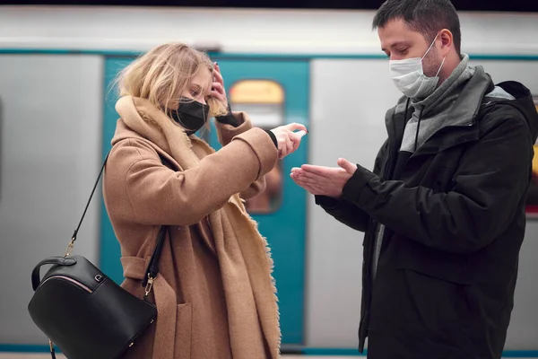 Hombre y mujer en máscaras médicas usando antiséptico mientras están de pie cerca de vagón subterráneo — Foto de Stock