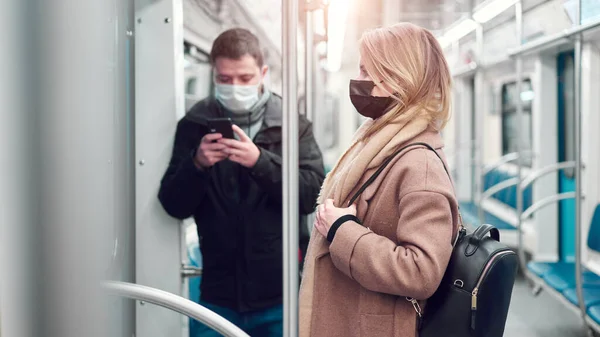 Brunet man with phone in hands and woman in medical masks standing in subway car. — Stock Photo, Image