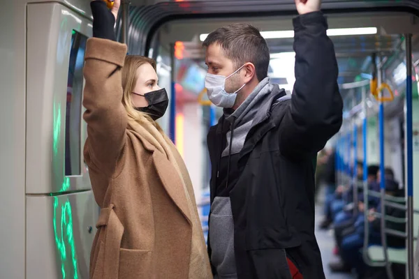 Man and woman in medical masks holding handrails in subway car — Stock Photo, Image