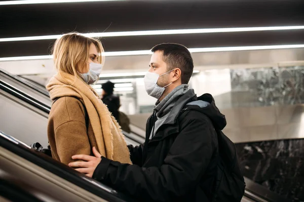 Boční pohled na mladý pár v lékařských maskách na eskalátoru v metru. — Stock fotografie