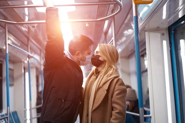 Egy fiatal pár orvosi maszkban korlátokat tart a metrókocsiban. Coronavirus pandémia. — Stock Fotó