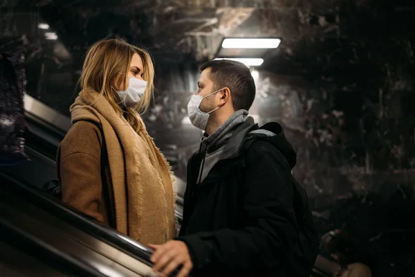 Молодий чоловік і жінка дивляться один на одного в медичних масках на ескалаторі в метро . — стокове фото