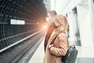 Tıbbi maskeli genç bir adam ve kadın metroda at arabasının yanında dikiliyorlar. Koronavirüs salgını.