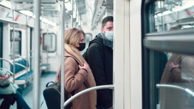 Tıbbi maskeli bir adam ve kadın metro vagonunda duruyor..