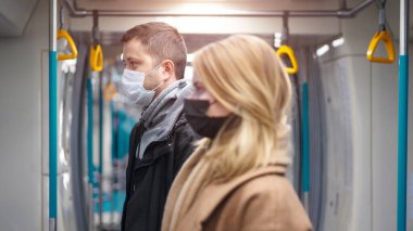 Tıbbi maskeli kadın ve erkeğin yan görüntüsü metro vagonunun yanında duruyor..