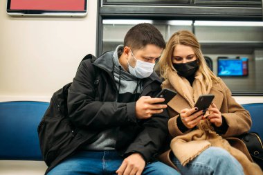 Ellerinde telefonlar olan bir adam ve bir kadın metroda oturuyor..