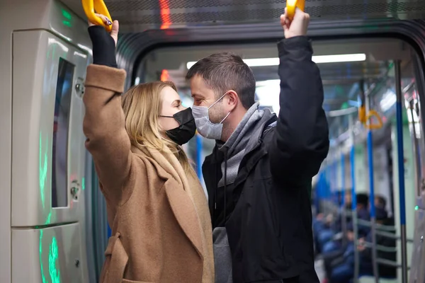 Mladý pár v lékařských maskách drží zábradlí v autě metra. — Stock fotografie