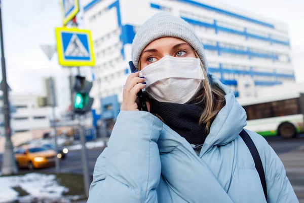 Молода жінка в масці розмовляє по телефону на прогулянці по вулиці в місті вдень . — стокове фото