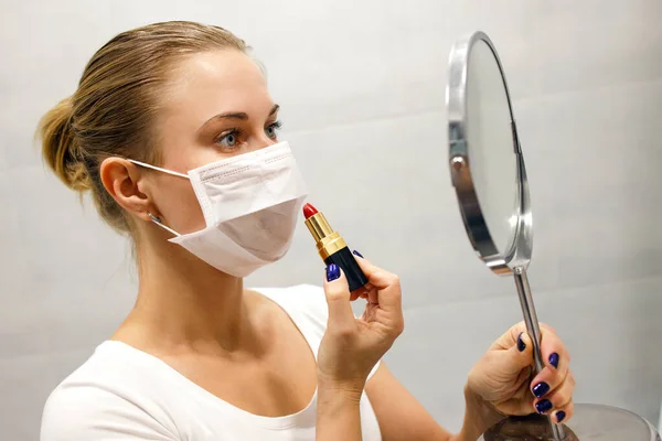 Close-up van jong blond in medisch masker met lippenstift en spiegel in haar hand — Stockfoto