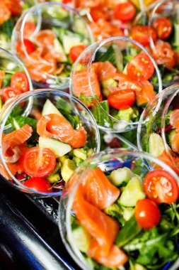 İçinde kırmızı balık salatası, domates ve salatalık olan açık büfe masası.