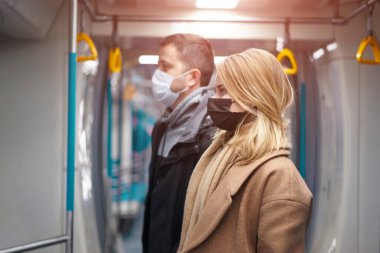 Tıbbi maskeli genç bir adam ve kadın metro vagonunun yanında dikiliyorlar..