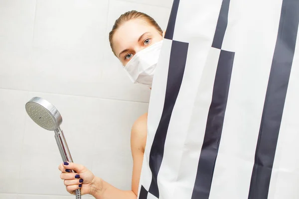 Close-up van jong blond in medisch masker staan in de douche naast gestreept gordijn — Stockfoto