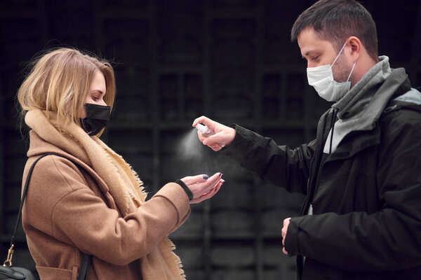 Young couple in medical masks using antiseptic carriage.