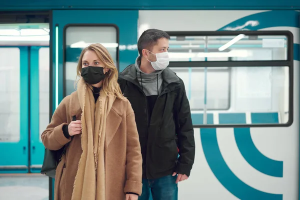 Tıbbi maskeli genç adam ve sarışın kadın metroda arabanın yanında duruyorlar.