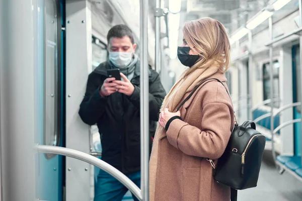 Homem com telefone nas mãos e mulher em máscaras médicas de pé no carro do metrô . — Fotografia de Stock