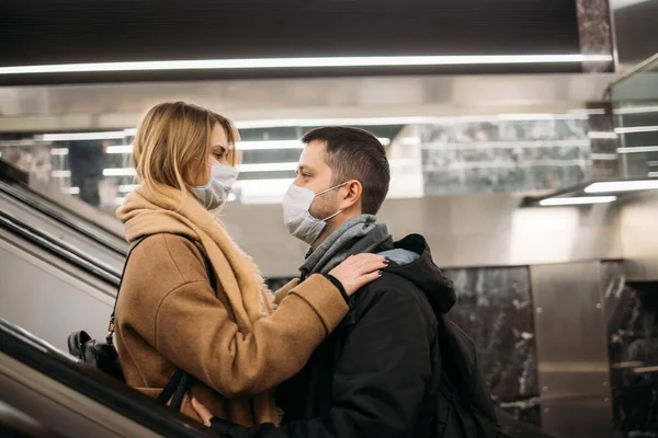 Vista lateral de la pareja de abrazos en máscaras médicas en escaleras mecánicas en el metro . — Foto de Stock