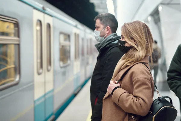 Vista lateral del joven hombre y la mujer en máscaras médicas de pie cerca del carro en el metro — Foto de Stock