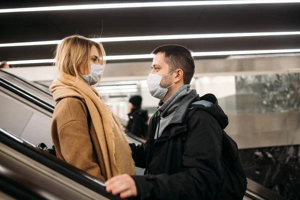Πλευρική άποψη του ζευγαριού αγάπης με ιατρικές μάσκες στις κυλιόμενες σκάλες στο μετρό. Πανδημία του Coronavirus. — Φωτογραφία Αρχείου