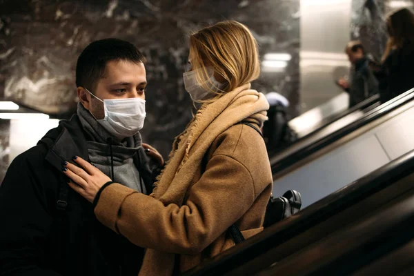 Joven hombre y mujer con máscaras médicas en escaleras mecánicas en el metro. pandemia de Coronavirus . — Foto de Stock