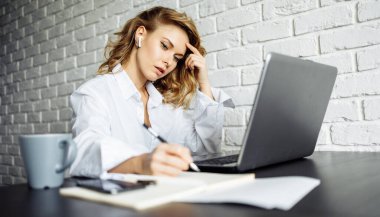 Kadın laptopla masada otururken bilgi yazıyor..