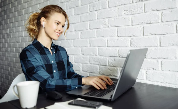 Mujer feliz freelancer sentado en la mesa con el ordenador portátil en el fondo de la pared de ladrillo blanco — Foto de Stock