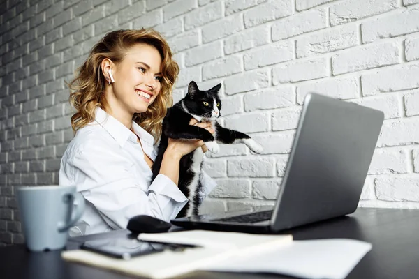 Young woman with black cat in her arms sitting at table with laptop