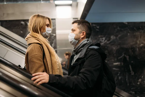 Vista lateral de abraçar homem e mulher em máscaras médicas na escada rolante no metrô . — Fotografia de Stock