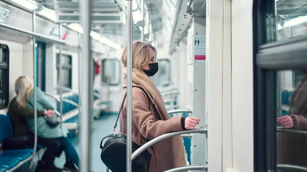 Chica rubia en máscara médica negro de pie en el coche del metro . — Foto de Stock