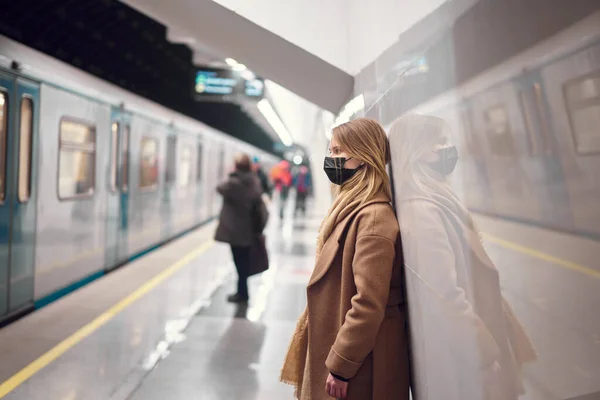 Wanita bertopeng medis hitam berdiri di kereta bawah tanah dekat kereta. — Stok Foto
