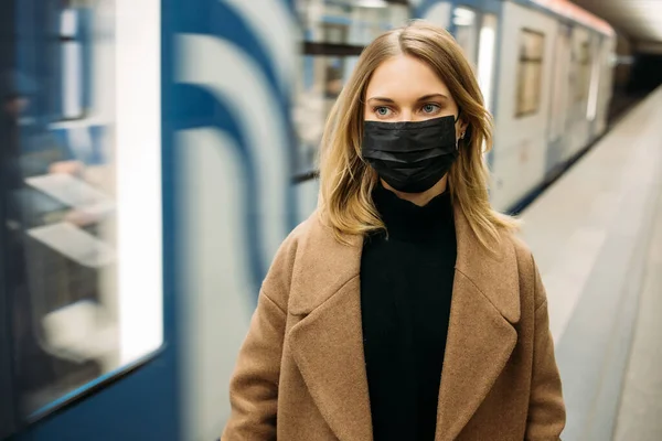 Молодь у чорній медичній масці дивиться на камеру, стоячи біля машини метро.. — стокове фото