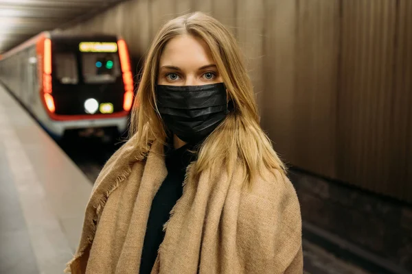 地下鉄の車の横に立っている間、黒の医療マスクの女の子はカメラを見て — ストック写真