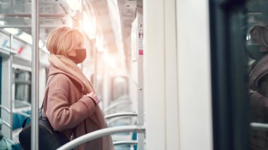 Siyah tıbbi maskeli genç bir kadın metronun yanında duruyor..