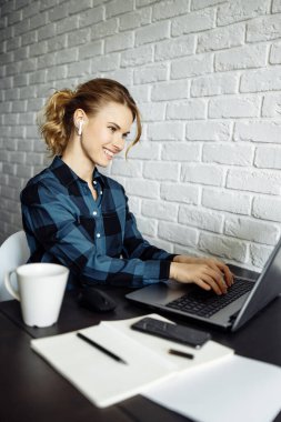 Masada dizüstü bilgisayarı beyaz tuğla duvarın arkasında oturan mutlu serbest çalışan kız.