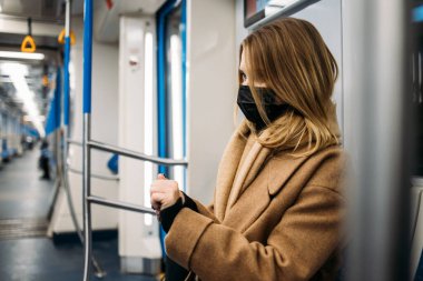 Tıbbi maskeli bir kız metroda arabada otururken ellerini dezenfekte ediyor..