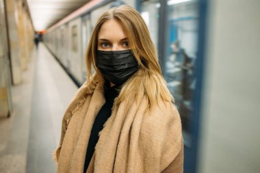 Siyah tıbbi maskeli kadın metro vagonunun yanında duruyor..