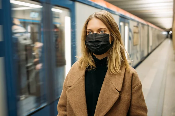 Блондинка в чорній медичній масці дивиться на камеру, стоячи поруч з машиною метро . — стокове фото